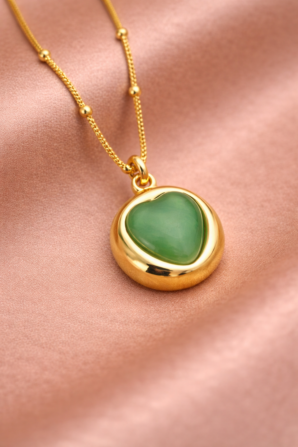 Close-up detail of Sivorae gold heart pendant necklace featuring smooth green stone and polished finish.