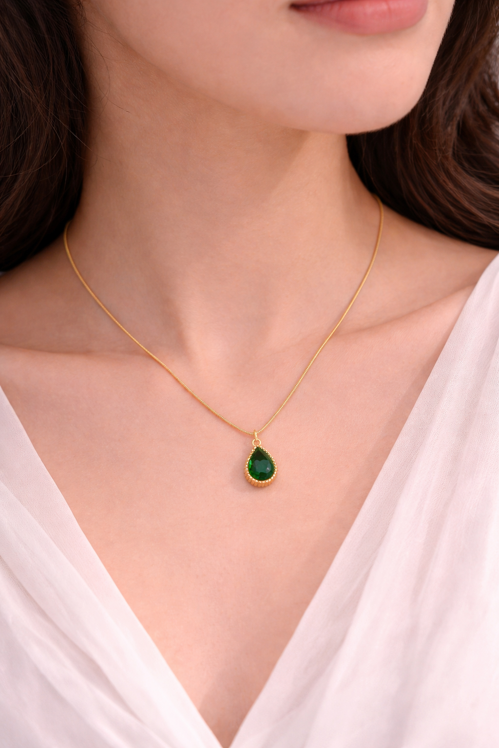 Woman wearing Sivorae steel golden chain necklace with emerald green teardrop pendant and halo design