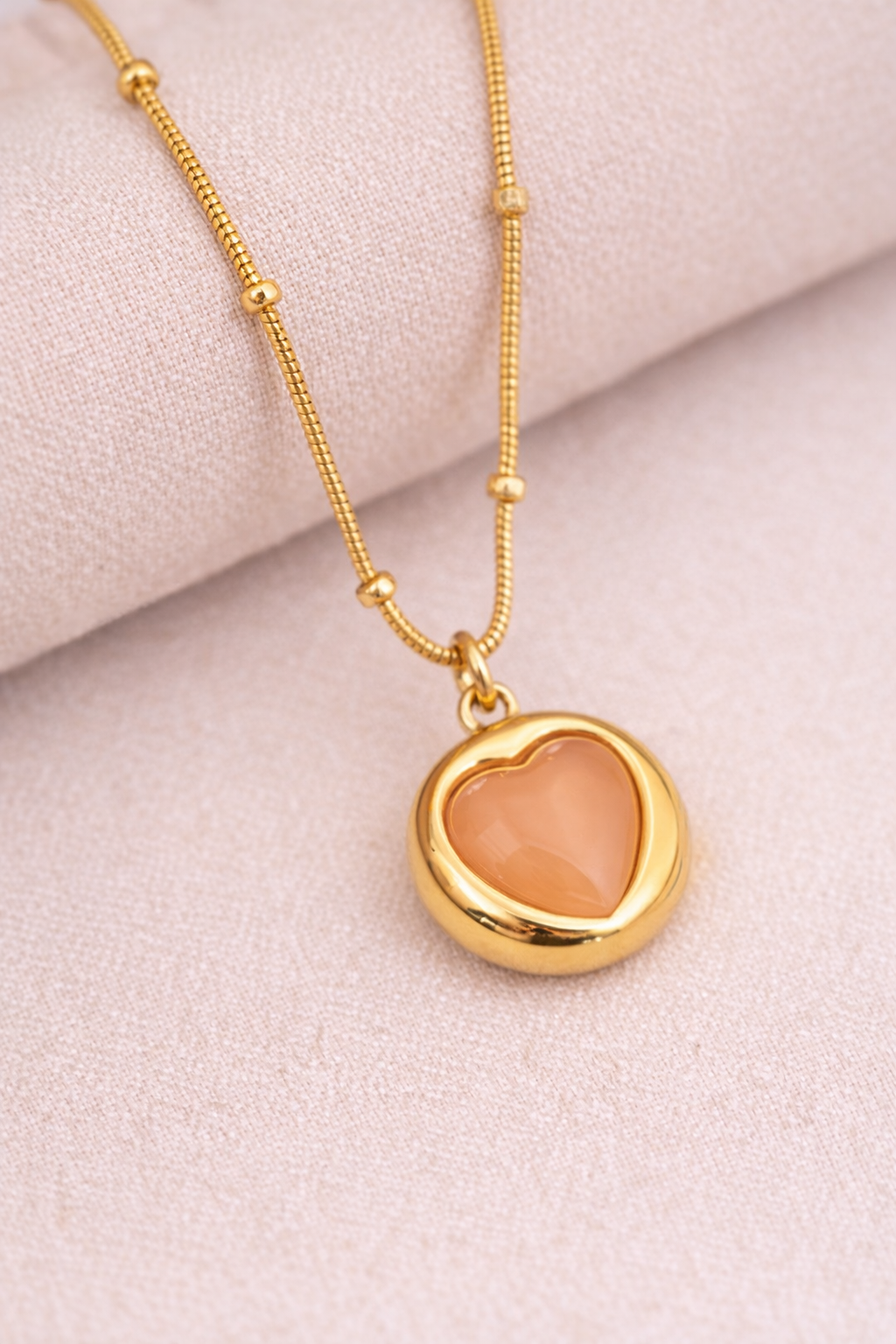 Close up of Sivorae steel golden heart pendant necklace showing peach stone and gold polished finish